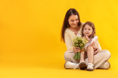 Photo of Mother and her little daughter with bouquet of beautiful chamomile flowers on orange background, space for text