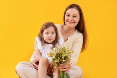 Photo of Mother and her little daughter with bouquet of beautiful chamomile flowers on orange background