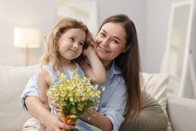 Photo of Mother and her little daughter with bouquet of beautiful chamomile flowers on sofa indoors