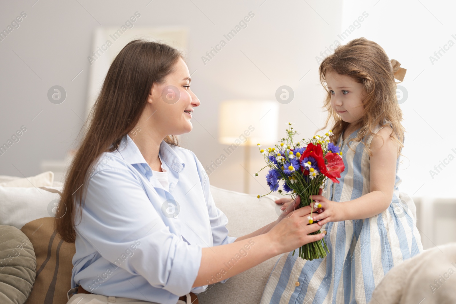 Photo of Mother and her little daughter with bouquet of beautiful flowers on sofa indoors