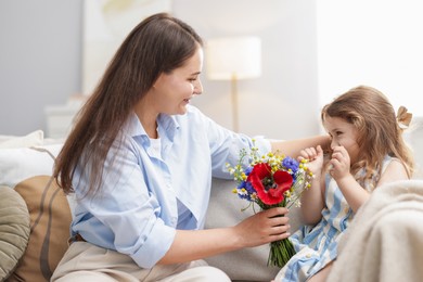 Photo of Mother and her little daughter with bouquet of beautiful flowers on sofa indoors