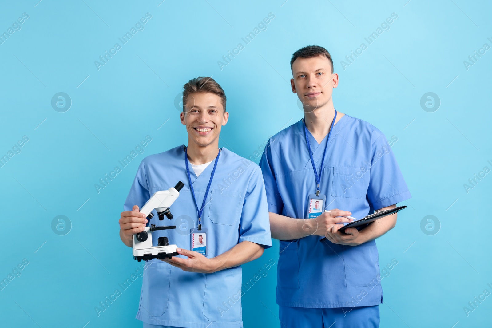 Medical students with microscope and clipboard on light blue background Photo of Medical students with microscope and clipboard on light blue background
