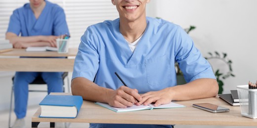 Photo of Medical students in uniforms studying at desks indoors, selective focus