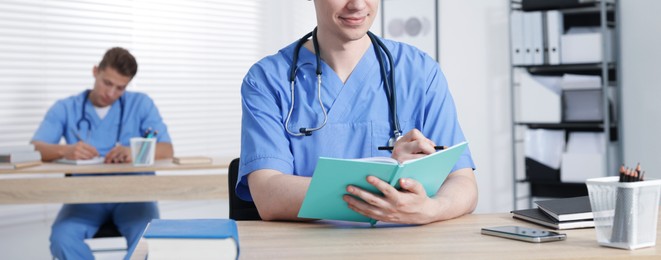 Photo of Medical students in uniforms studying at desks indoors, selective focus