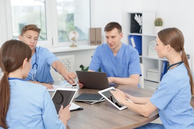 Photo of Medical students in uniforms studying together at table indoors