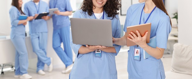 Photo of Medical students in uniforms with tablet and laptop indoors, selective focus