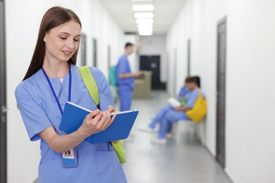 Photo of Medical student in uniform with backpack and notebook indoors, selective focus
