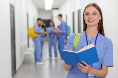 Photo of Medical student in uniform with backpack and notebook indoors, selective focus