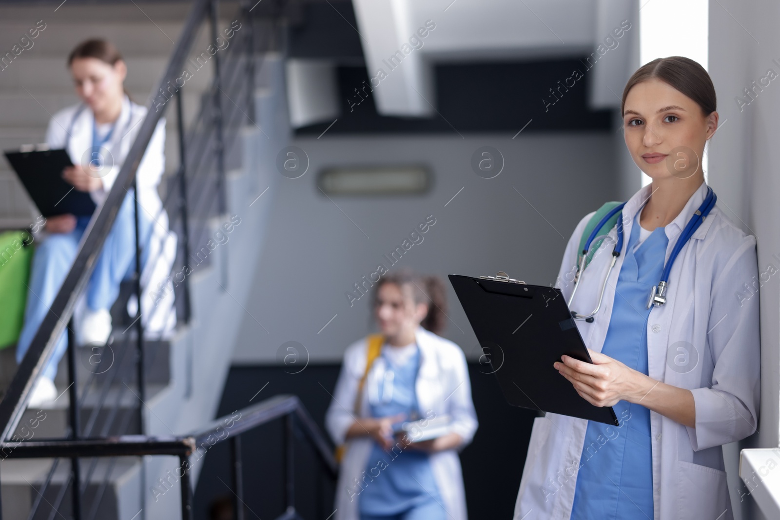 Photo of Medical student in uniform with clipboard and stethoscope on stairs indoors, selective focus