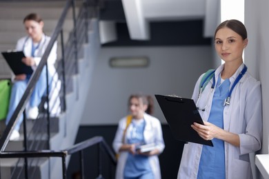 Photo of Medical student in uniform with clipboard and stethoscope on stairs indoors, selective focus