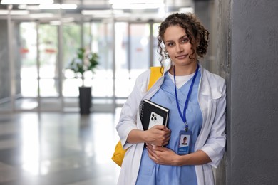 Photo of Medical student in uniform with notebook and smartphone indoors, space for text