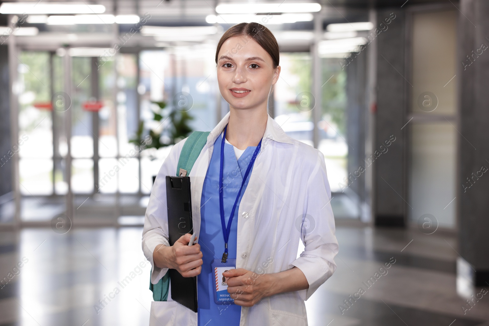 Medical student in uniform with backpack and clipboard indoors Photo of Medical student in uniform with backpack and clipboard indoors