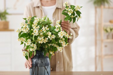 Photo of Woman making bouquet of jasmine branches at wooden table, closeup