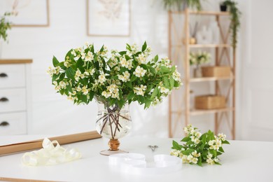Photo of Bouquet of beautiful jasmine flowers in vase on white table indoors