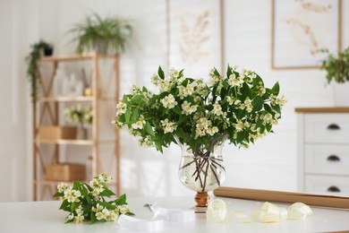 Photo of Bouquet of beautiful jasmine flowers in vase on white table indoors