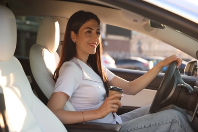 Photo of Woman with coffee behind steering wheel of modern car