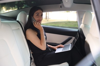 Photo of Woman with laptop talking on smartphone in modern car, view from outside