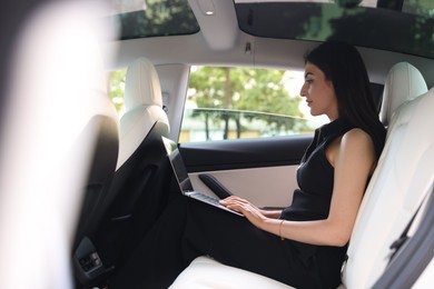 Photo of Woman using laptop in modern car, view from outside