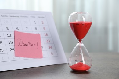 Photo of Sticky note with word Deadline, calendar and hourglass with flowing sand on wooden table indoors, closeup