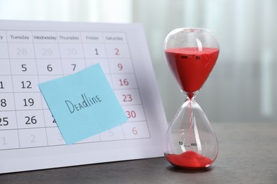 Photo of Sticky note with word Deadline, calendar and hourglass with flowing sand on wooden table indoors, closeup