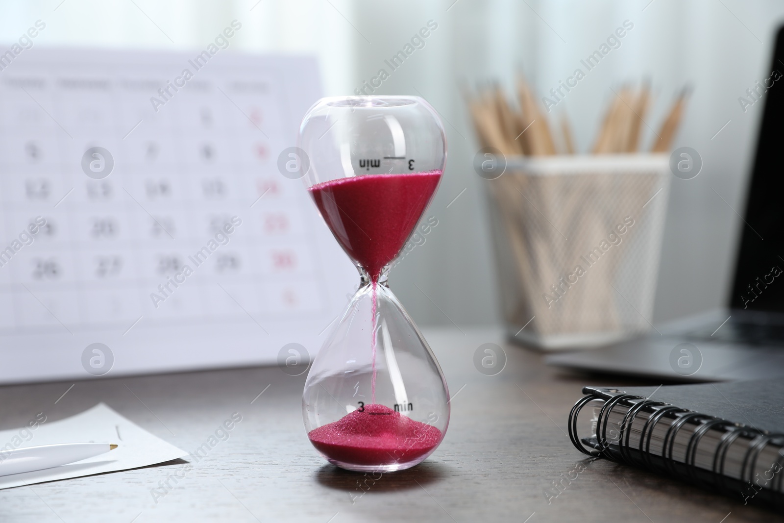 Photo of Deadline. Hourglass with flowing sand, stationery, calendar and laptop on wooden table indoors