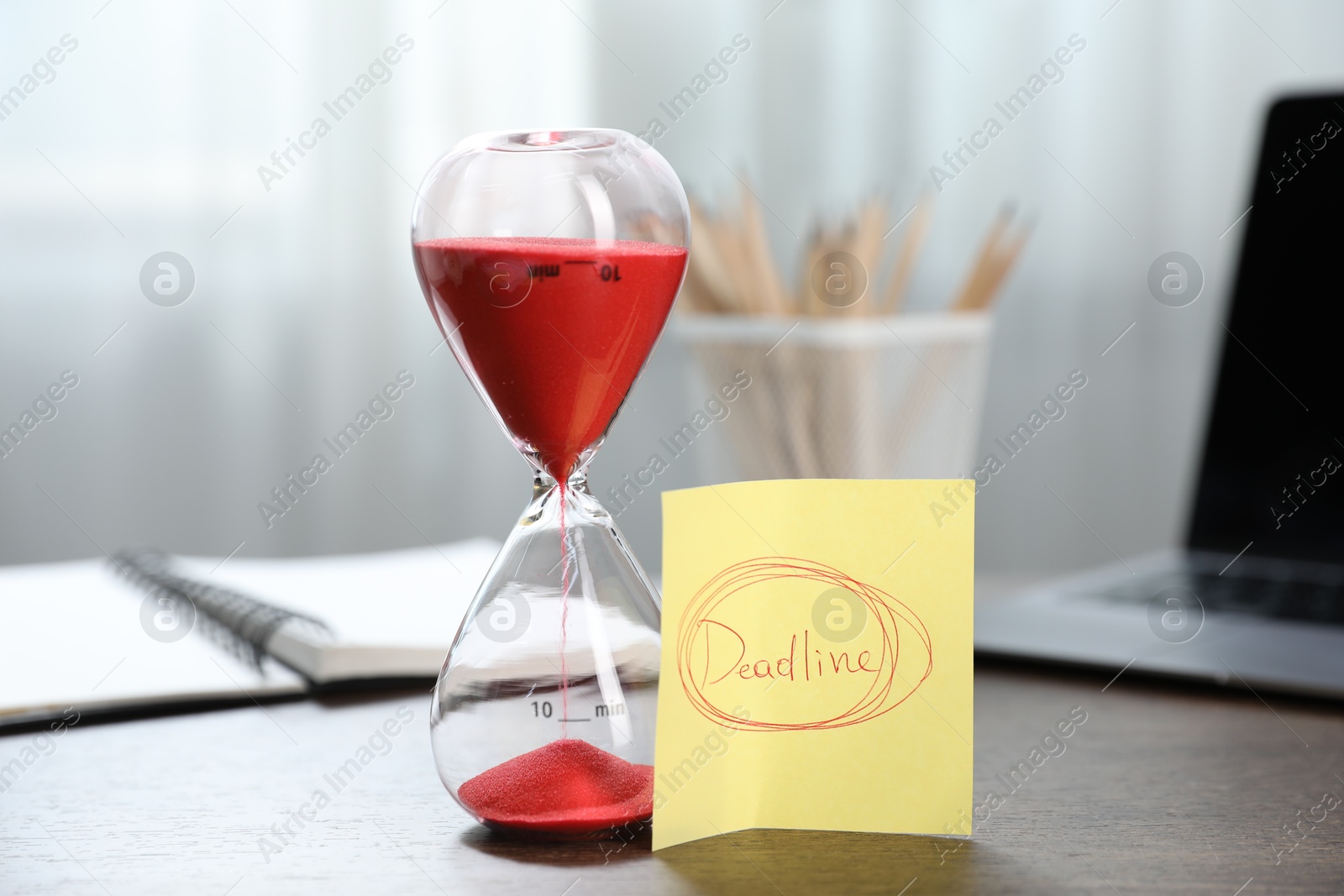 Sticky note with word Deadline, hourglass, stationery and laptop on wooden table indoors, closeup Photo of Sticky note with word Deadline, hourglass, stationery and laptop on wooden table indoors, closeup