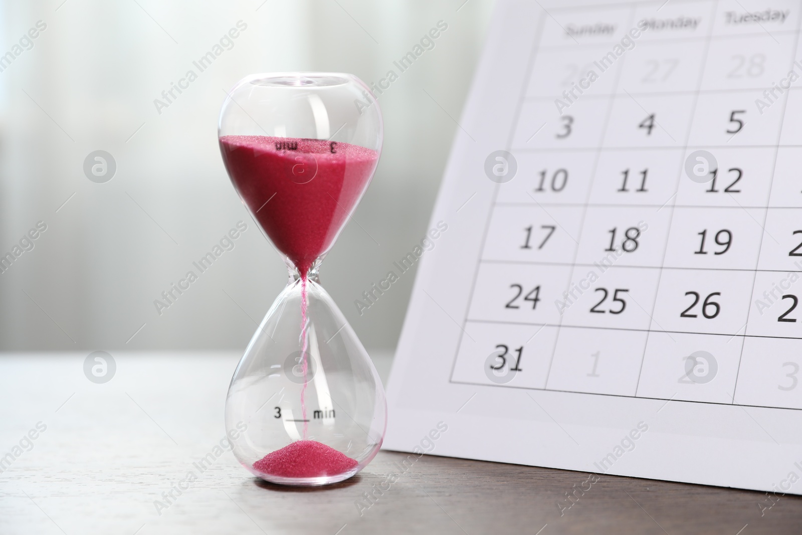 Deadline. Hourglass with flowing sand and calendar on wooden table indoors, closeup Photo of Deadline. Hourglass with flowing sand and calendar on wooden table indoors, closeup