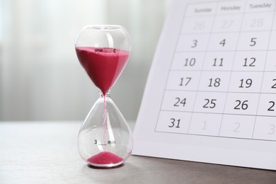 Photo of Deadline. Hourglass with flowing sand and calendar on wooden table indoors, closeup