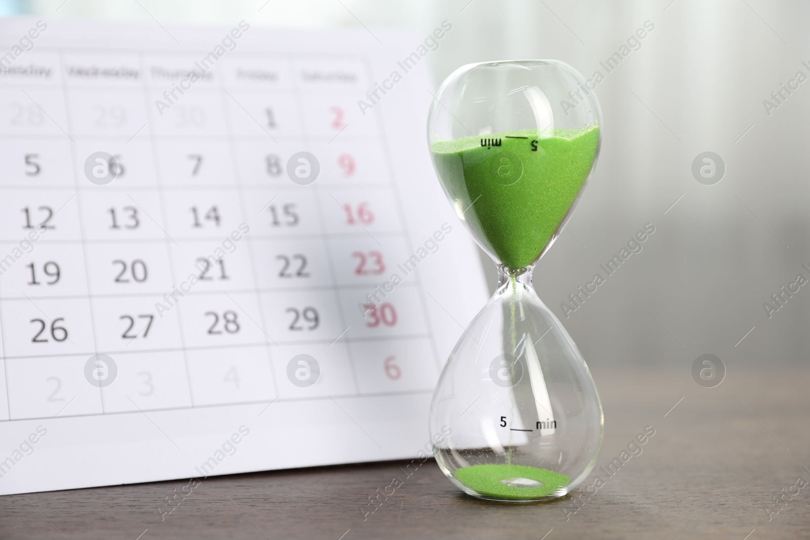 Deadline. Hourglass with flowing sand and calendar on wooden table indoors, closeup Photo of Deadline. Hourglass with flowing sand and calendar on wooden table indoors, closeup