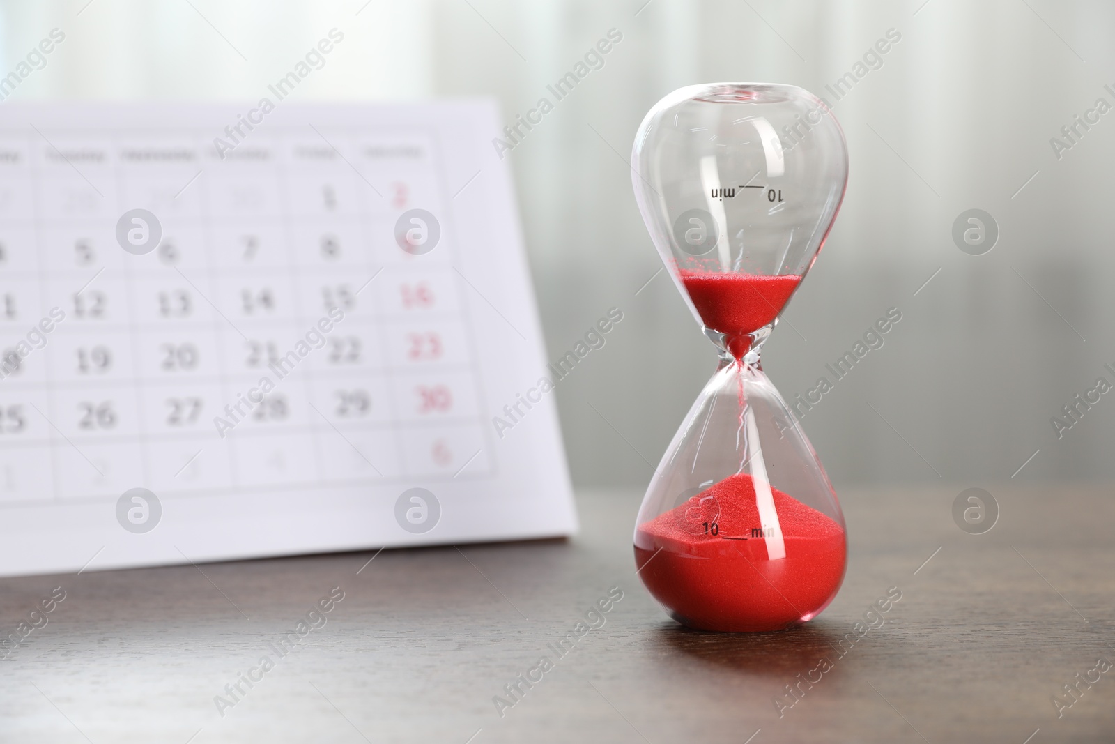Deadline. Hourglass with flowing sand and calendar on wooden table indoors Photo of Deadline. Hourglass with flowing sand and calendar on wooden table indoors
