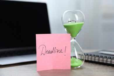Photo of Sticky note with word Deadline, hourglass, notebook and laptop on wooden table indoors, closeup