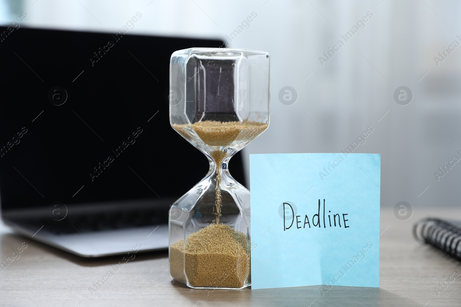 Sticky note with word Deadline, hourglass and laptop on wooden table indoors, closeup Photo of Sticky note with word Deadline, hourglass and laptop on wooden table indoors, closeup