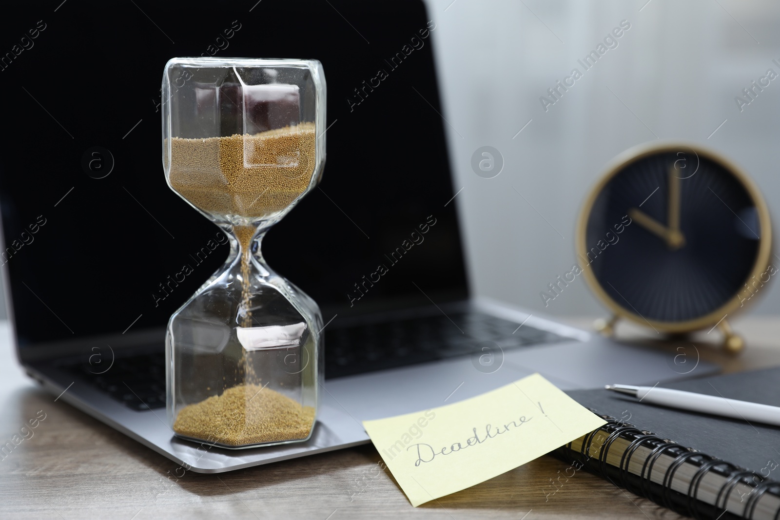Sticky note with word Deadline, hourglass, alarm clock, stationery and laptop on wooden table indoors, closeup Photo of Sticky note with word Deadline, hourglass, alarm clock, stationery and laptop on wooden table indoors, closeup