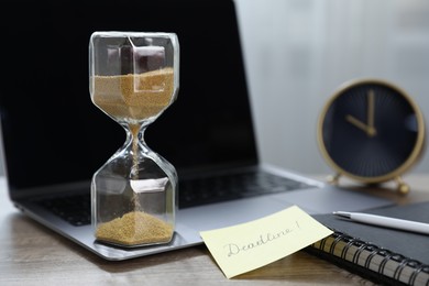 Photo of Sticky note with word Deadline, hourglass, alarm clock, stationery and laptop on wooden table indoors, closeup