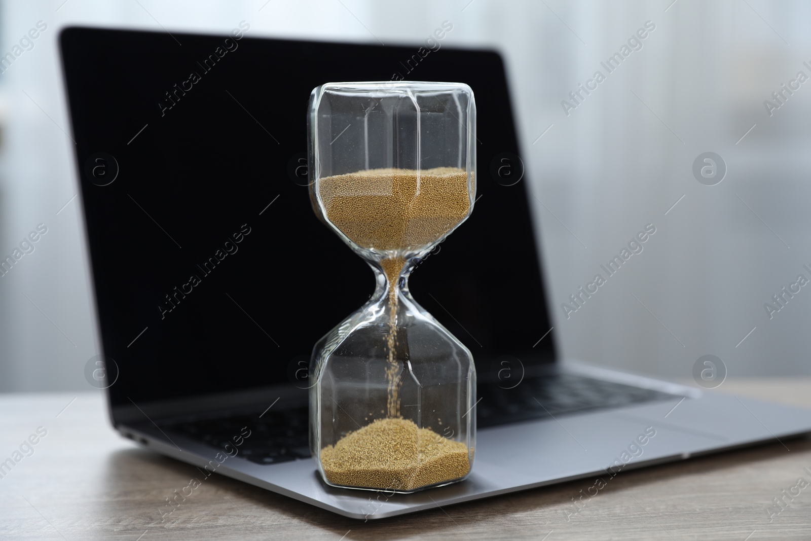Deadline. Hourglass with flowing sand and laptop on wooden table indoors, closeup Photo of Deadline. Hourglass with flowing sand and laptop on wooden table indoors, closeup