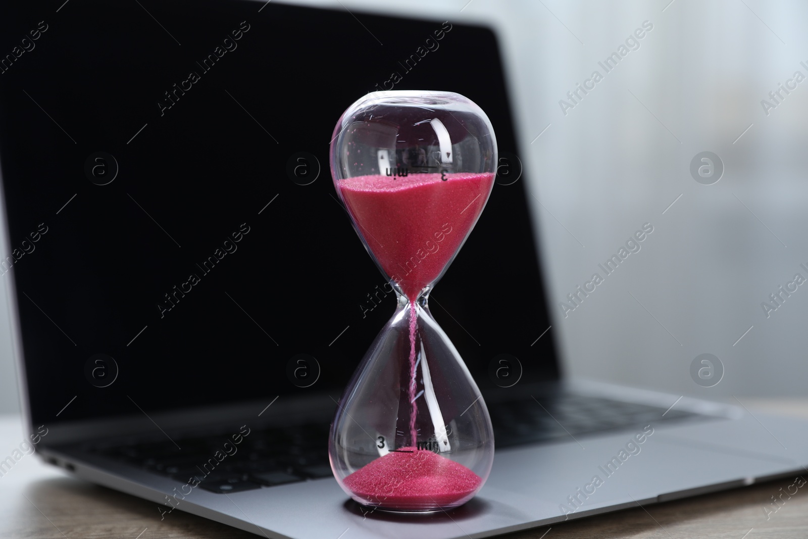 Deadline. Hourglass with flowing sand and laptop on table indoors, closeup Photo of Deadline. Hourglass with flowing sand and laptop on table indoors, closeup
