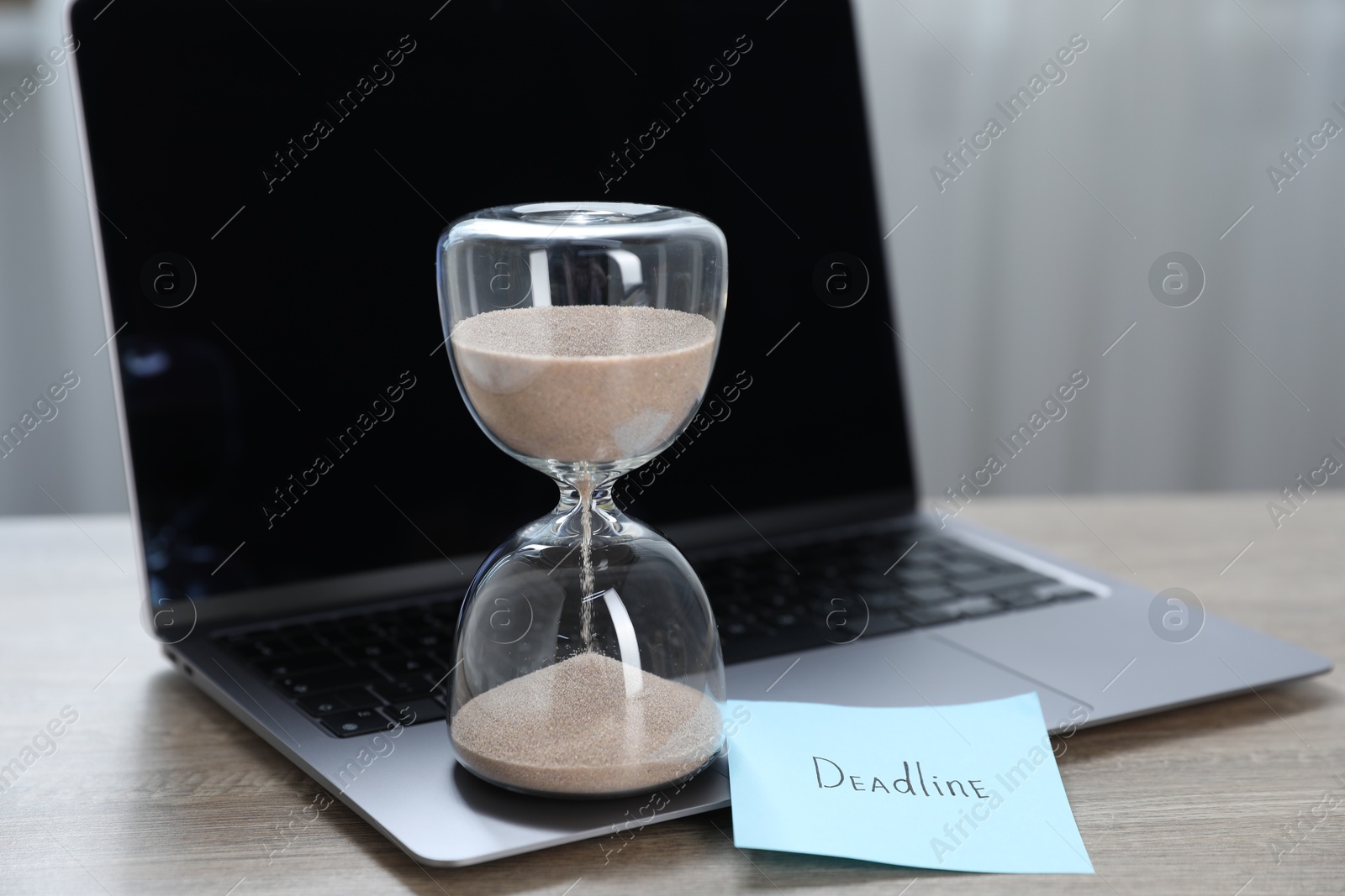 Sticky note with word Deadline, hourglass and laptop on wooden table indoors, closeup Photo of Sticky note with word Deadline, hourglass and laptop on wooden table indoors, closeup
