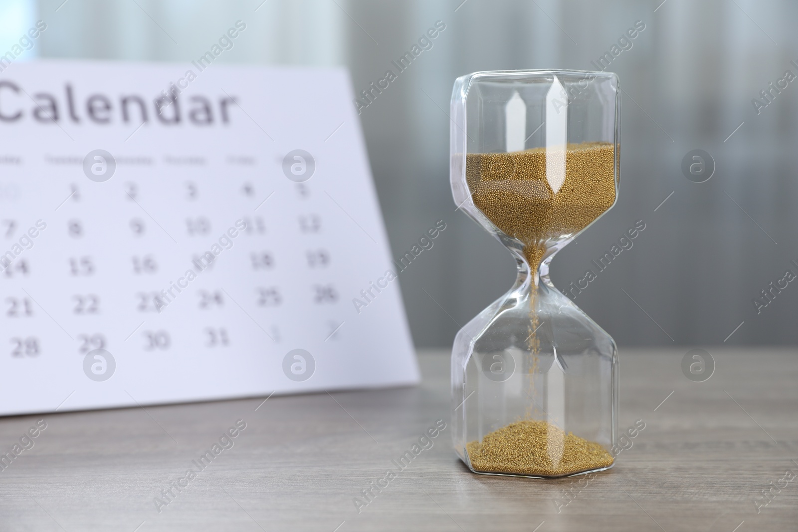 Deadline. Hourglass with flowing sand and calendar on wooden table indoors Photo of Deadline. Hourglass with flowing sand and calendar on wooden table indoors