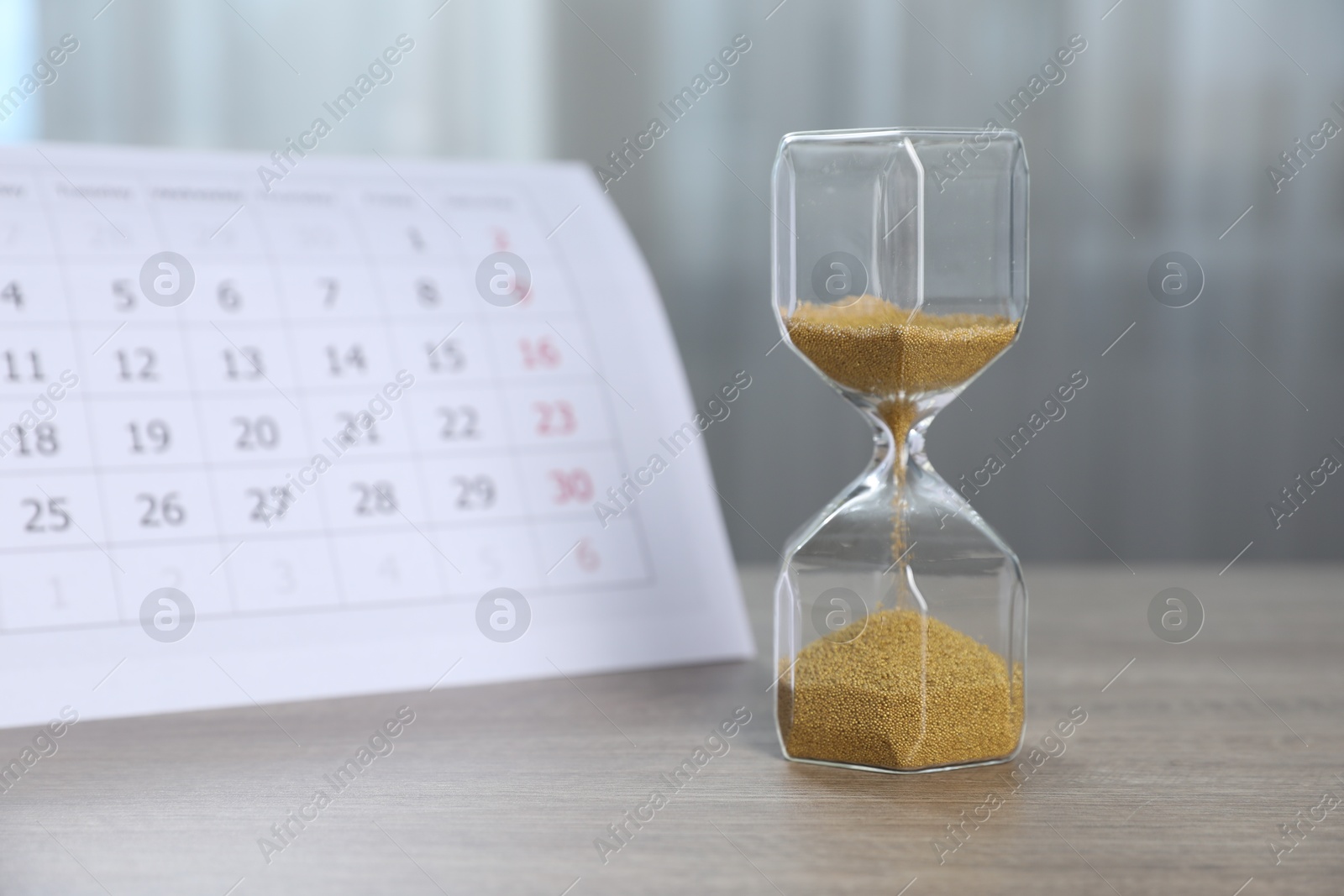 Deadline. Hourglass with flowing sand and calendar on wooden table indoors Photo of Deadline. Hourglass with flowing sand and calendar on wooden table indoors