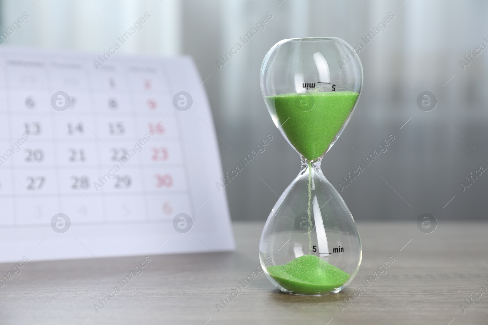 Deadline. Hourglass with flowing sand and calendar on wooden table indoors Photo of Deadline. Hourglass with flowing sand and calendar on wooden table indoors