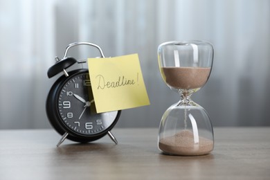 Photo of Sticky note with word Deadline, hourglass and alarm clock on wooden table indoors
