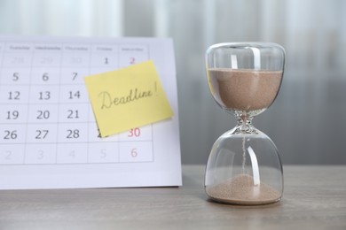 Photo of Sticky note with word Deadline, hourglass and calendar on wooden table indoors