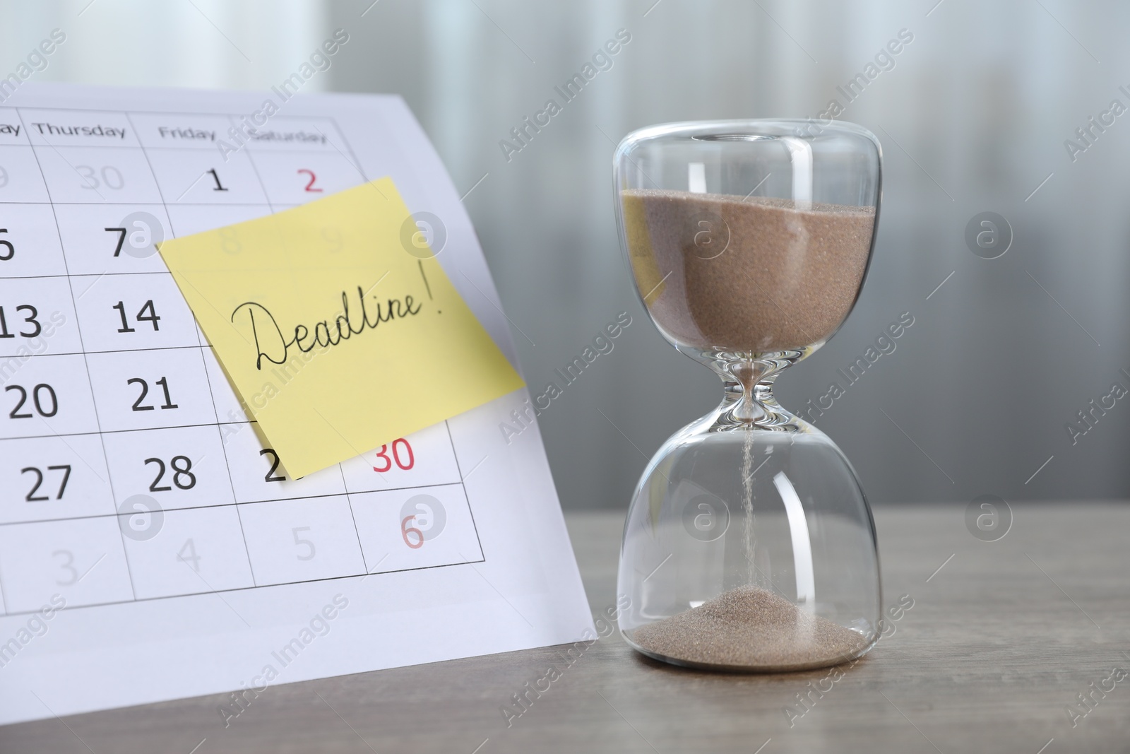 Sticky note with word Deadline, hourglass and calendar on wooden table indoors, closeup Photo of Sticky note with word Deadline, hourglass and calendar on wooden table indoors, closeup