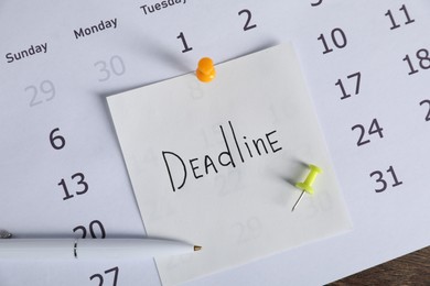 Photo of Sticky note with word Deadline, calendar and pen on table, top view