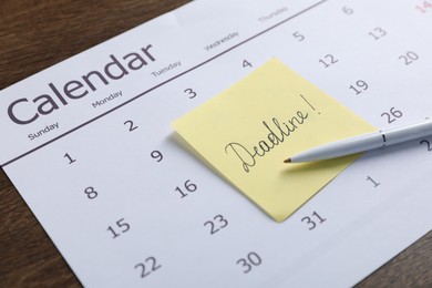 Photo of Sticky note with word Deadline, calendar and pen on wooden table, closeup