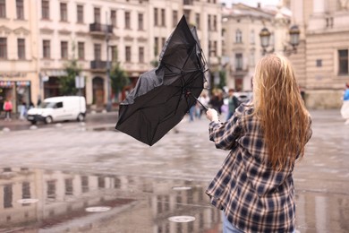 Photo of Woman with broken umbrella on city street, back view. Space for text