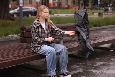 Photo of Woman with broken umbrella on bench outdoors