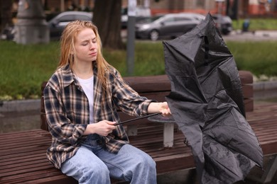 Photo of Woman with broken umbrella on bench outdoors