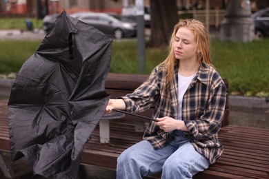 Photo of Woman with broken umbrella on bench outdoors