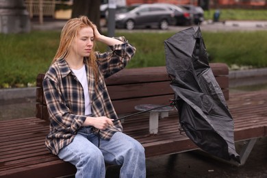 Photo of Frustrated woman with broken umbrella on bench outdoors